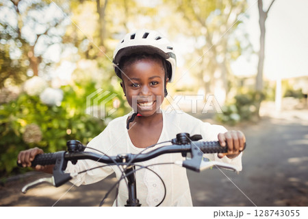 African American child gripping bicycle handlebars while wearing protective helmet on suburban road 128743055