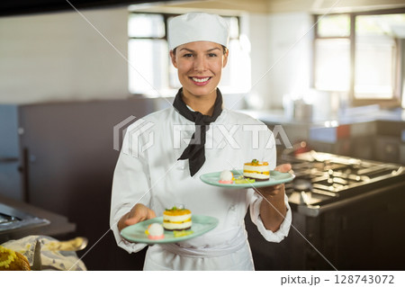 Mid adult chef presenting layered desserts on plates in restaurant kitchen, showing culinary skill Mid adult chef presenting layered desserts on plates in restaurant kitchen, showing culinary skill 128743072
