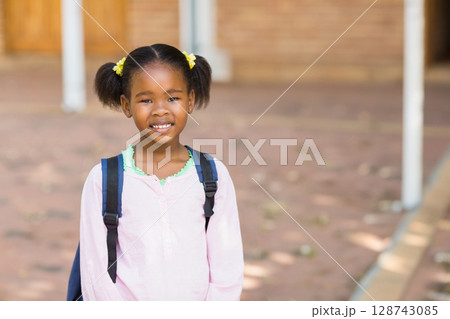 African American girl standing and smiling in brick school courtyard, carrying dark backpack African American girl standing and smiling in brick school courtyard, carrying dark backpack 128743085