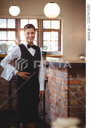 Woman bartender leaning on brick counter inside bar café, smiling beside pendant lamps, copy space 128743105