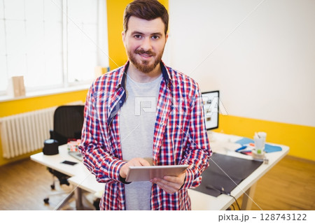 Male office worker holding tablet in modern office, with computer monitor, mouse pad and coffee cup 128743122
