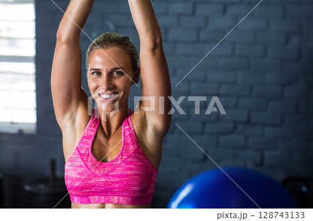 Mid adult woman raising arms overhead in gym, with blue exercise ball and weight stacks Mid adult woman raising arms overhead in gym, with blue exercise ball and weight stacks 128743133