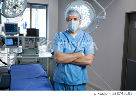 Senior male surgeon standing in operating room, with table, lights, anesthesia machine and monitors 128743195