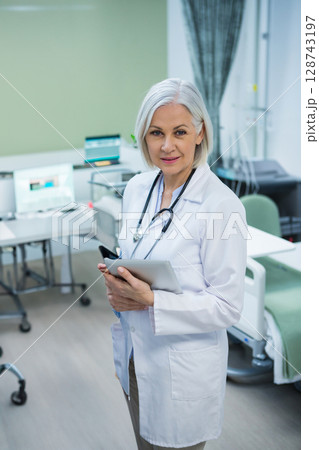 Female doctor holding tablet and wearing stethoscope in exam room, showing attentive focus 128743197