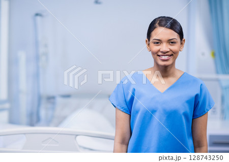 Woman in scrubs smiling in hospital room, with bed rails, IV stand, medical panel, copy space Woman in scrubs smiling in hospital room, with bed rails, IV stand, medical panel, copy space 128743250