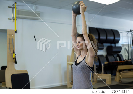 Young adult African American woman holding medicine ball overhead in Pilates studio, copy space 128743314