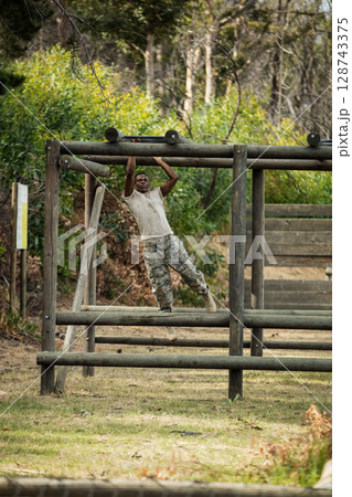 African American man hanging from wooden beams in wooded training area, with wooden ramp 128743375