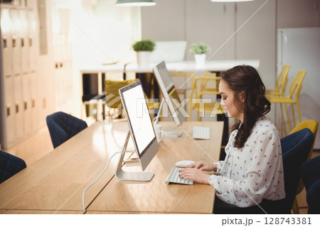 Asian woman typing on wireless keyboard in modern co-working space, with coffee mug, copy space Asian woman typing on wireless keyboard in modern co-working space, with coffee mug, copy space 128743381
