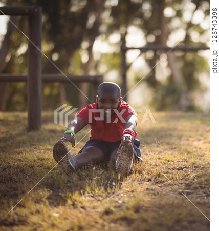 African American boy stretching forward on dry grass in park by wooden bars, wearing wristbands African American boy stretching forward on dry grass in park by wooden bars, wearing wristbands 128743398