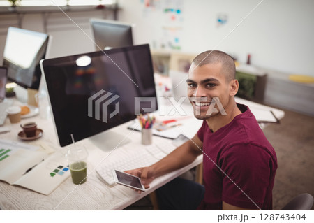 Man sitting at office desk holding smartphone with monitor, charts and color swatches, copy space Man sitting at office desk holding smartphone with monitor, charts and color swatches, copy space 128743404