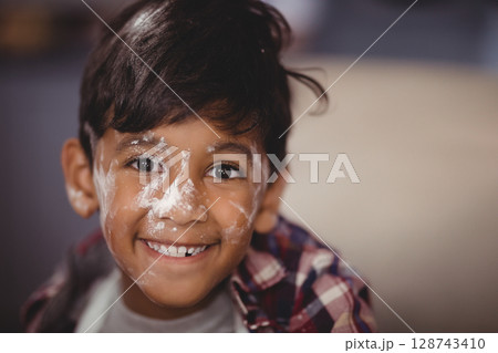 Indian boy smiling at camera at home, showing white flour on face and plaid shirt 128743410