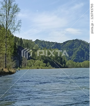 Scenic Riverscape with Lush Forest and Mountain Backdrop Under a Bright Blue Sky Scenic Riverscape with Lush Forest and Mountain Backdrop Under a Bright Blue Sky 128743793