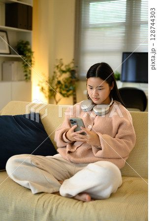 Teenager with wireless headphones around her neck, texting or scrolling on her phone 128744303