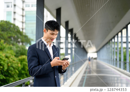 Businessman in formal suit checking his smartphone on a modern pedestrian bridge 128744353