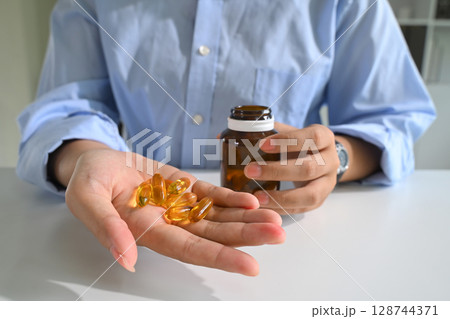 Close up of a person holding fish oil capsules in one hand. Health and nutrition concept 128744371