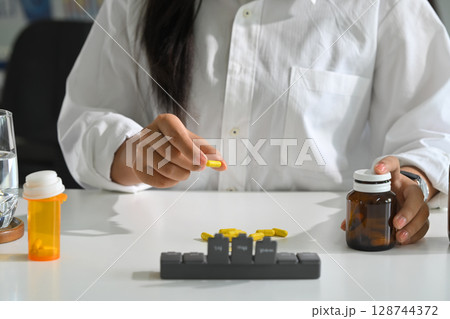 Woman organizing capsules into weekly pill box, daily medication management and routine Woman organizing capsules into weekly pill box, daily medication management and routine 128744372