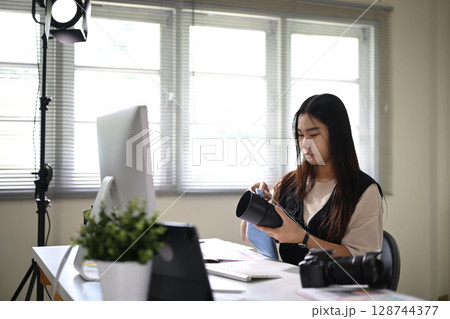 Female photographer cleaning a camera lens at her workstation Female photographer cleaning a camera lens at her workstation 128744377