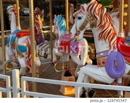 Brightly painted carousel horses are arranged in a circle, ready for riders at a festive event during the beautiful evening hours Brightly painted carousel horses are arranged in a circle, ready for riders at a festive event during the beautiful evening hours 128745347