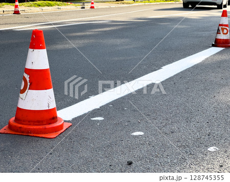 Traffic cones are placed along freshly painted lines on a bustling city street as cars navigate around them during the day Traffic cones are placed along freshly painted lines on a bustling city street as cars navigate around them during the day 128745355