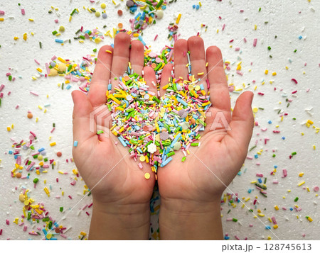 Sugar fine confectionery sprinkles form a heart shape in the palms of a child. Conceptual photo on a white background. 128745613
