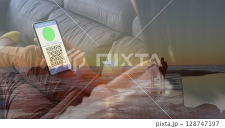 Image of woman with covid passport on smartphone over couple on beach 128747197
