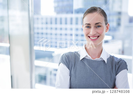 Businesswoman in business attire standing arms crossed on balcony with glass railing, copy space 128748108