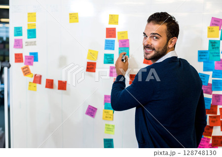 Man in sweater writing with marker on office whiteboard full of neon sticky notes, copy space 128748130