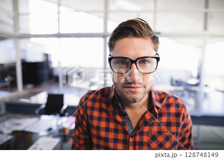 Man standing in modern office wearing glasses and plaid shirt with desks and monitors Man standing in modern office wearing glasses and plaid shirt with desks and monitors 128748149