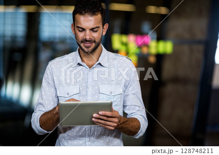 Male professional holding tablet and studying colorful notes on glass partition at modern office 128748211