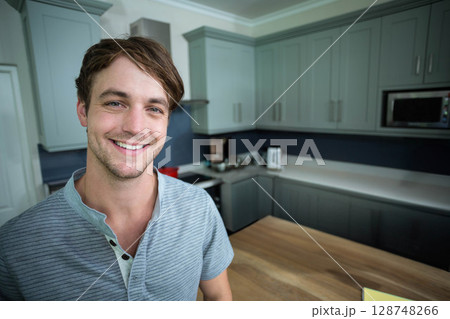 Man smiling and standing beside countertop island in home kitchen near toaster kettle and microwave 128748266