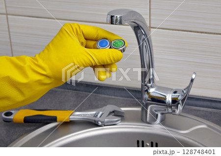yellow gloved hands fixing a faucet in the kitchen 128748401