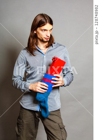 Guy putting wrapped gift in knitted christmas sock 128748982