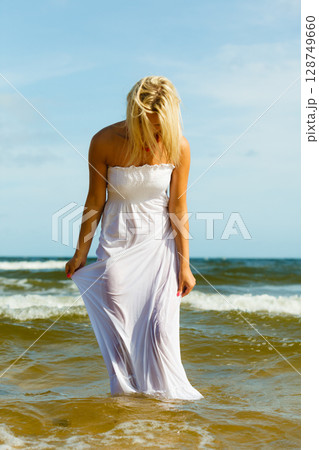 Blonde woman wearing dress walking in water Blonde woman wearing dress walking in water 128749660