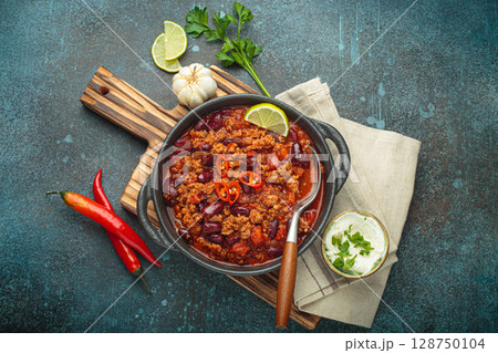 Mexican Chili con carne with minced meat, red beans, tomatoes, lime, and spices in a cast iron pot 128750104