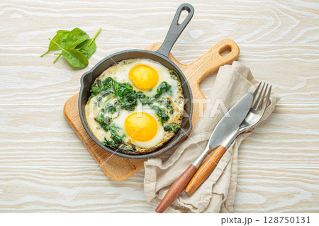 Healthy spinach omelette with two fried eggs in cast iron pan top view Healthy spinach omelette with two fried eggs in cast iron pan top view 128750131