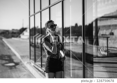 A girl with a long braided ponytail stands outside a glass building, holding her phone to her ear A girl with a long braided ponytail stands outside a glass building, holding her phone to her ear 128750678