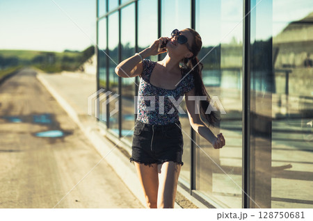 A girl with a ponytail stands near a glass building, smiling slightly as she talks 128750681