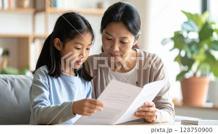 日本の小学生の女の子が保護者と一緒に家庭教師の広告を真剣に見つめる場面。教育、進路、親子の学習サポー 日本の小学生の女の子が保護者と一緒に家庭教師の広告を真剣に見つめる場面。教育、進路、親子の学習サポー 128750900