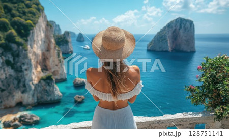 A woman in a straw hat stands on a balcony overlooking the ocean A woman in a straw hat stands on a balcony overlooking the ocean 128751141