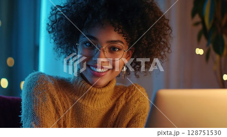 A woman who wears glasses is smiling while she uses her laptop 128751530