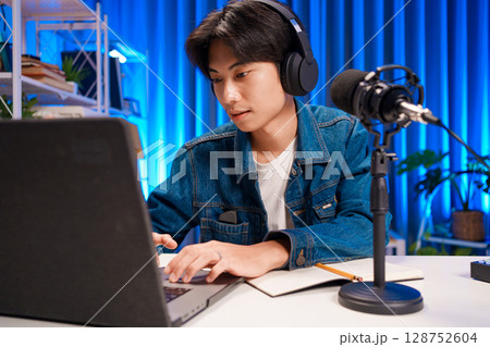 Smiling man podcaster make audio podcast with headphones and microphone in modern home studio. Smiling man podcaster make audio podcast with headphones and microphone in modern home studio. 128752604