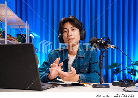 Smiling man podcaster make audio podcast with headphones and microphone in modern home studio. Smiling man podcaster make audio podcast with headphones and microphone in modern home studio. 128752615