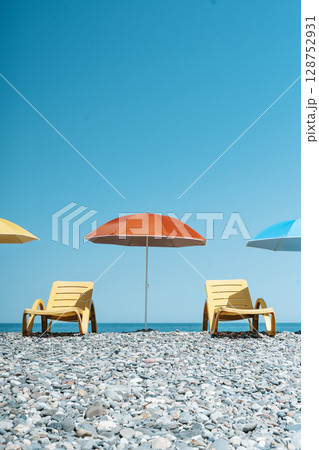 Colorful Beach Umbrellas and Sun Loungers on a Pebble Seaside 128752931