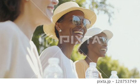 Three women enjoying walk in park with water, bright sunlight background 128753749