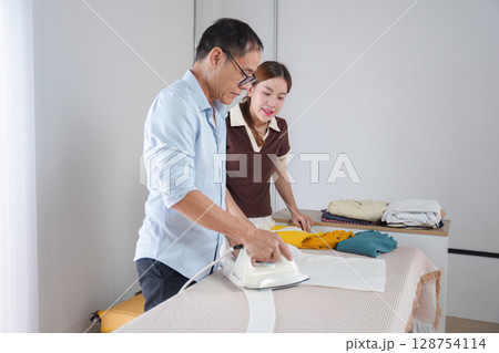 Father Teaching Daughter to Iron Clothes at Home - Family Bonding and Life Skills Learning in a Modern Household Setting Father Teaching Daughter to Iron Clothes at Home - Family Bonding and Life Skills Learning in a Modern Household Setting 128754114