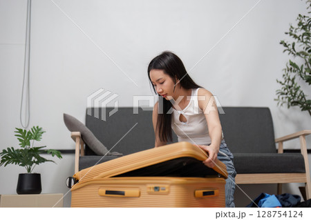 Young Woman Packing Suitcase for Travel Adventure in Modern Living Room Setting with Stylish Decor and Casual Clothing 128754124