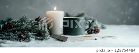 Lit candle and cup on book with pine branch for cozy Christmas festive winter setting 128754484