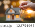 Hand holding house key in front of blurred model home at sunset 128754965