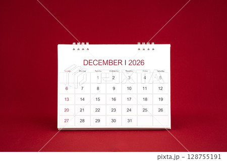 December 2026 white desk calendar stand on dark red color background. December 2026 white desk calendar stand on dark red color background. 128755191