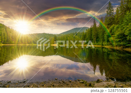 remote mountain landscape with forest lake in summer at sunset. travel nature background in evening light scenic view of coniferous trees reflection in water under the rainbow 128755501